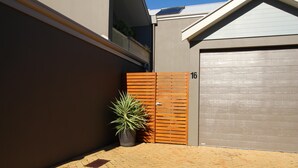 A modern building with a grey facade, a wooden gate marked with the number 16, and a potted plant in the foreground.