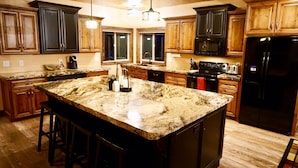 Una cocina con encimeras de granito, armarios de madera, un refrigerador negro y una isla grande con taburetes de bar.