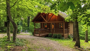 A log cabin with a porch, surrounded by trees and a gravel path. - Hot Tub, Fire Pit, Large Decks & Blackstone Griddle (Logan)