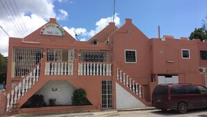 A pink building with a sign that reads "Hotel Magico." It has a staircase with white balustrades leading to a gated entrance. - La Bienvenue Rentals (Willemstad)