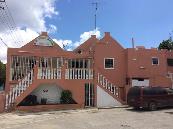 Un edificio rosa con un letrero que dice "Hotel Magico". Tiene una escalera con balaustradas blancas que conduce a una entrada con portón.