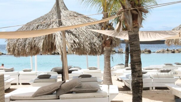A beachside lounge area with white lounge chairs and thatched umbrellas, overlooking a calm sea. - La Bienvenue Rentals (Willemstad)