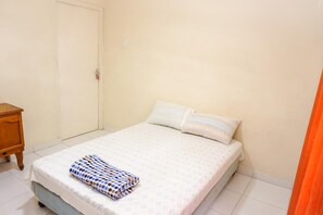 Un dormitorio pequeño y limpio con una cama individual, una mesita de noche de madera y una puerta blanca.