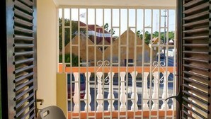 A balcony with a metal gate, a folding chair, and a view of a street with buildings. - La Bienvenue Rentals (Willemstad)