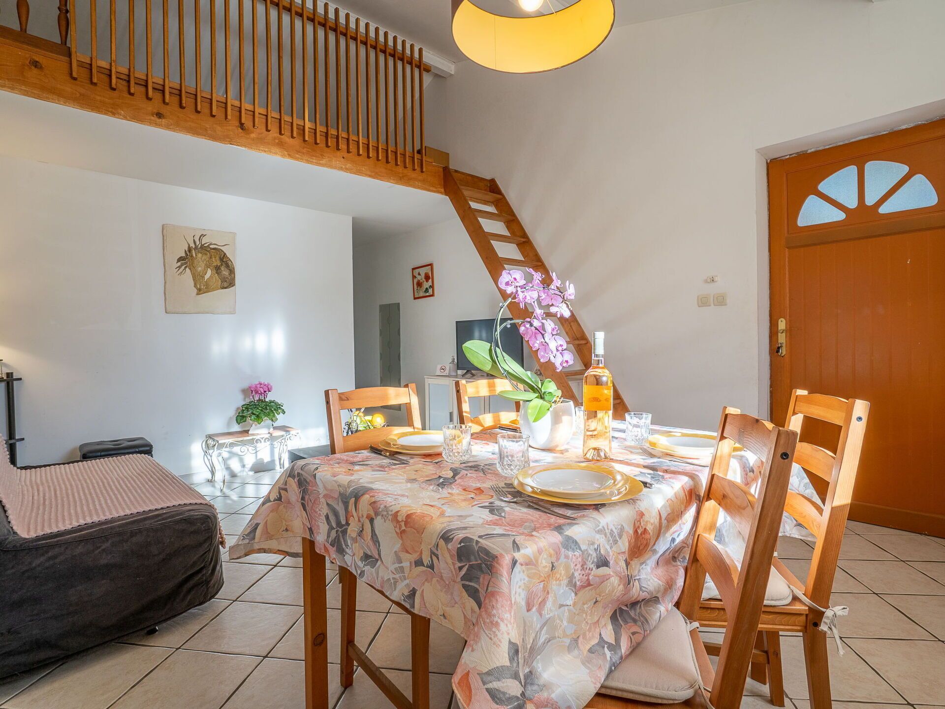 Un comedor con una mesa dispuesta para cuatro, sillas de madera, un sofá y una escalera.