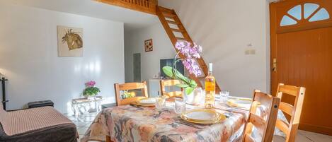 Un comedor con una mesa dispuesta para cuatro, sillas de madera, un sofá y una escalera.