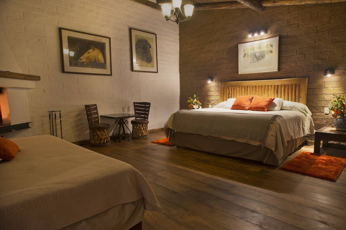 Una habitación de hotel con suelo de madera, una cama con cabecero, una mesa con sillas y cuadros en la pared.
