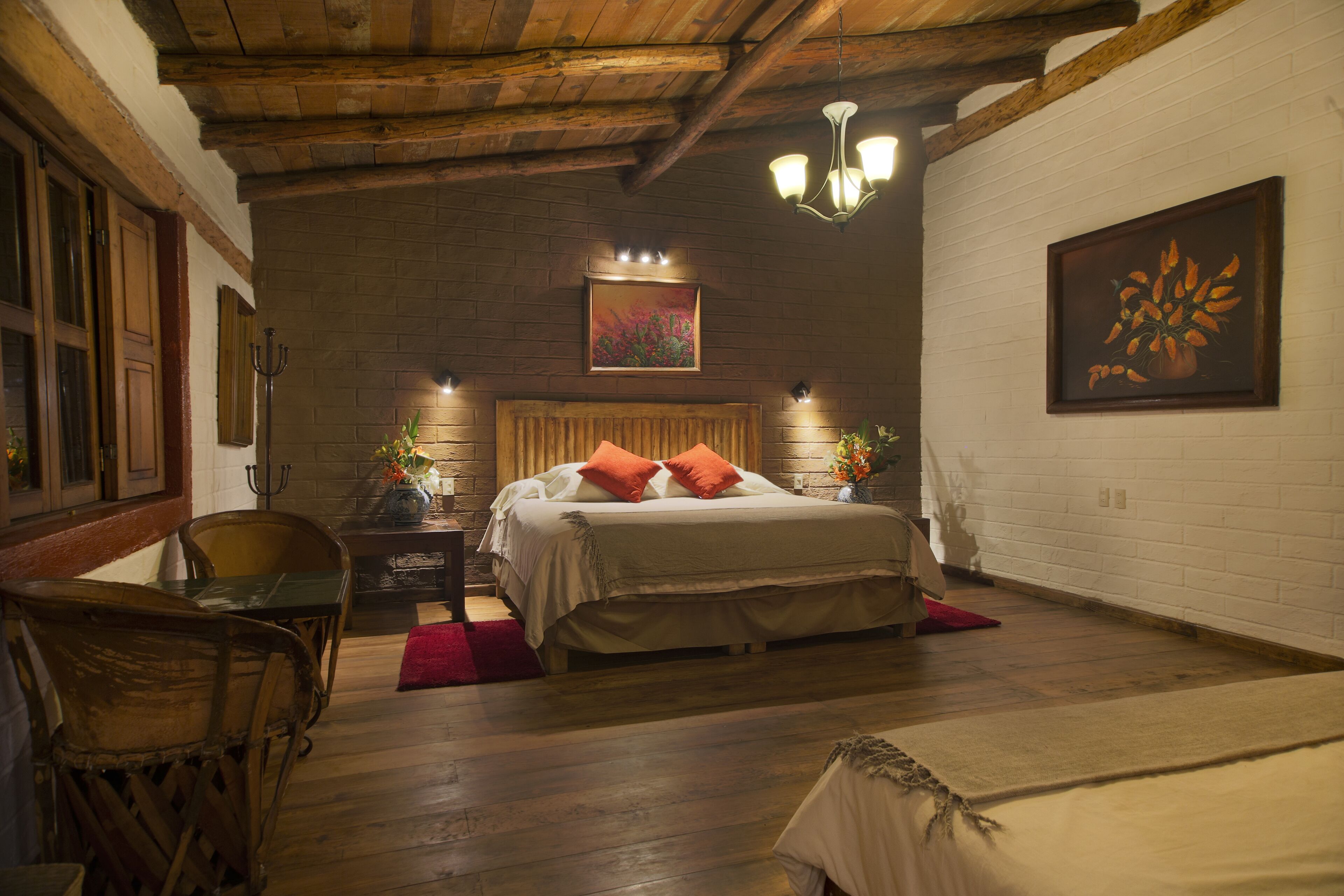A cozy room with a wooden ceiling, a bed with orange pillows, a table with chairs, and a painting on the wall.
