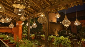 Une cour agrémentée de lampes en osier suspendues, de plantes en pot et d’une fontaine en pierre.