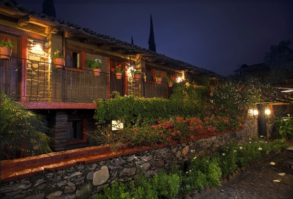 Un edificio de piedra tradicional con un balcón, plantas en macetas y un muro de piedra.