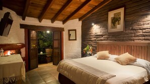 Une chambre confortable avec un grand lit, des poutres en bois, des murs en pierre et une petite table sur laquelle est posée une bougie.