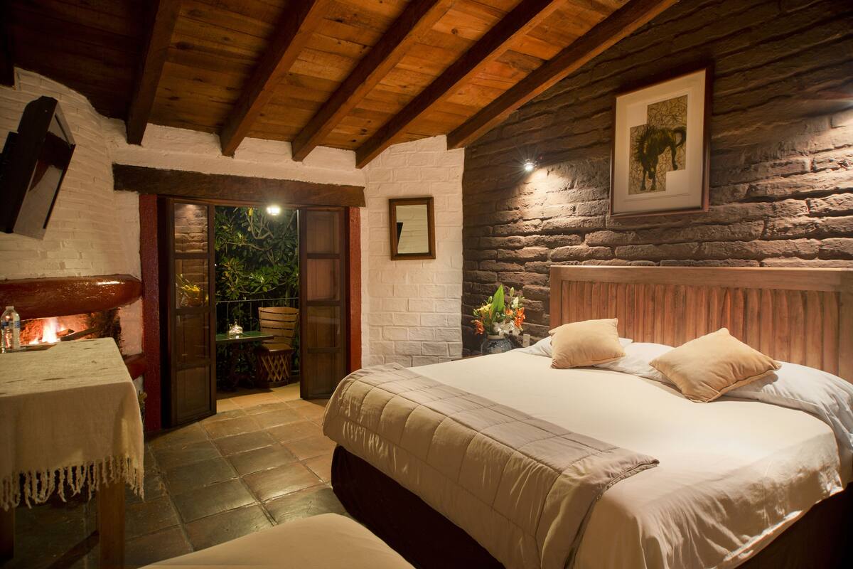 Un dormitorio acogedor con una cama grande, vigas de madera, paredes de piedra y una mesita con una vela.