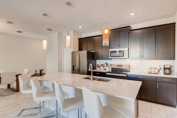 A modern kitchen with a central island, dark cabinets, stainless steel appliances, and pendant lighting.