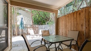 Un patio con tavolo e sedie in vetro, un recinto in legno e vista su un giardino sul retro.