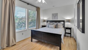 Una camera da letto con un letto, un ventilatore a soffitto, un comodino, una lampada e una finestra con tende.