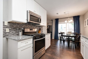 A modern kitchen with white cabinets, a stainless steel stove, and a microwave. There is a dining area with a table and chairs. - West Austin Extended Stay #2 by AustinGetaways (Austin)