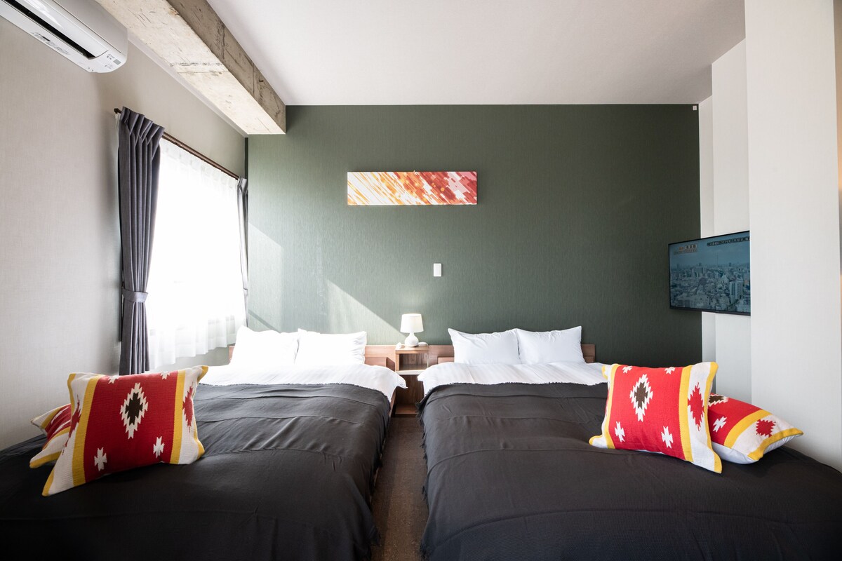 Habitación de hotel con dos camas, una mesita de noche, una lámpara y un cuadro en la pared.