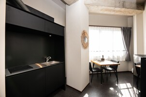 Cocina compacta con encimera negra, lavabo y zona de comedor con mesa y sillas.