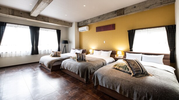 A hotel room with three beds, wooden beams on the ceiling, and large windows with curtains. - Volcano (Kagoshima)
