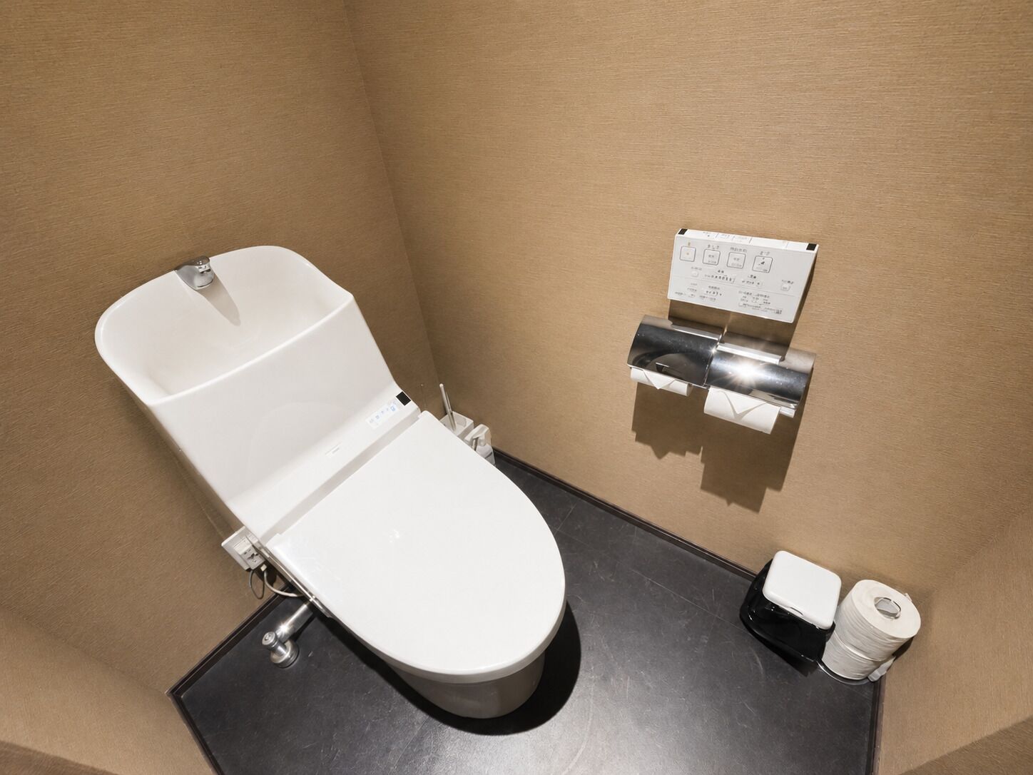 Une salle de bain moderne avec des toilettes blanches, un distributeur d’essuie-tout et un rouleau de papier toilette.