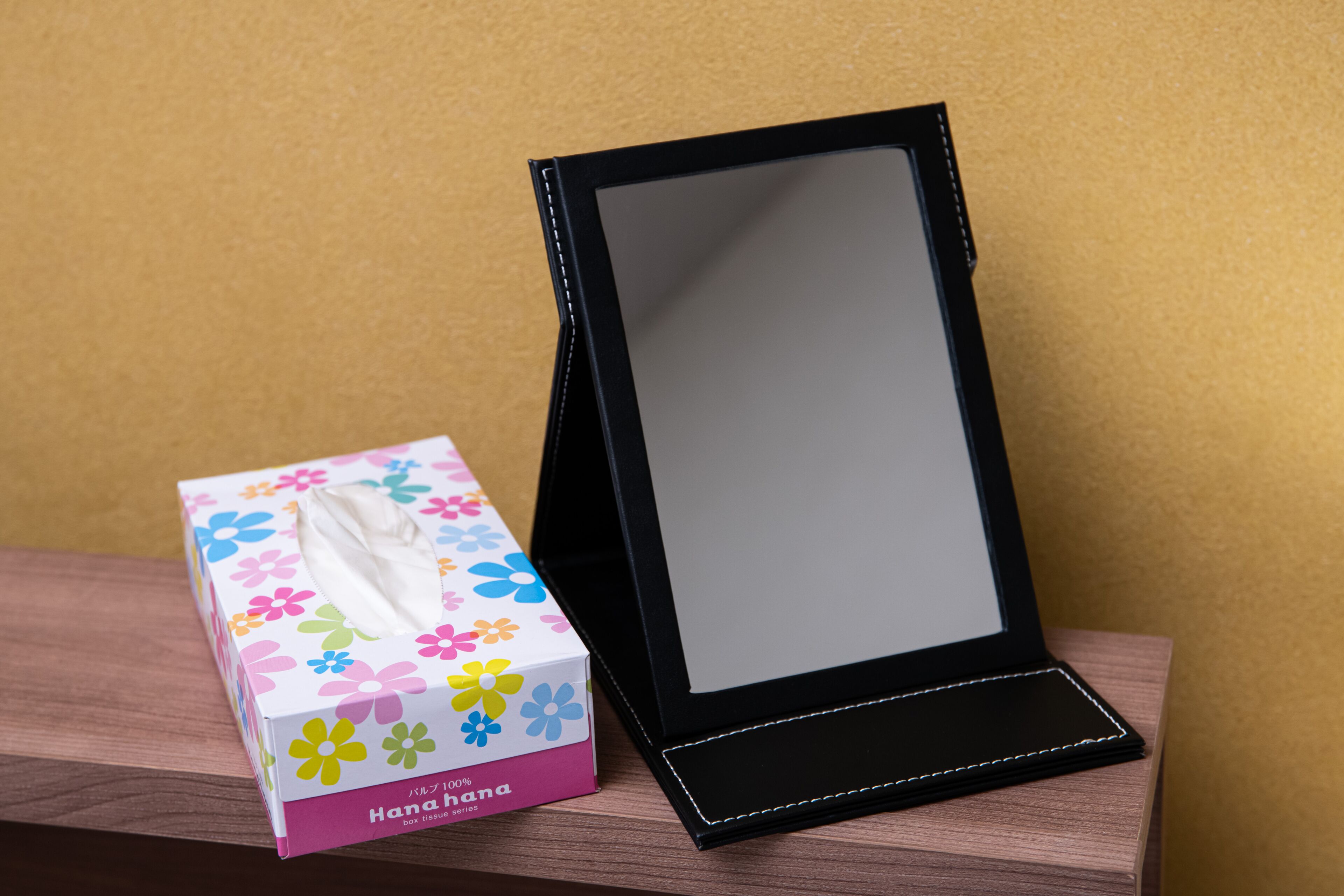 Une boîte de mouchoirs et un miroir à cadre noir, posés sur une surface en bois.