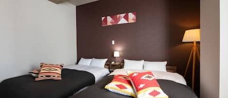 A hotel room with two beds, a wooden headboard, a wall-mounted lamp, and a geometric wall decoration.