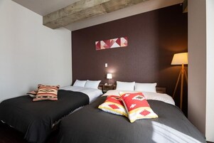 Habitación de hotel con dos camas, cabecero de madera, lámpara de pared y decoración geométrica en la pared.