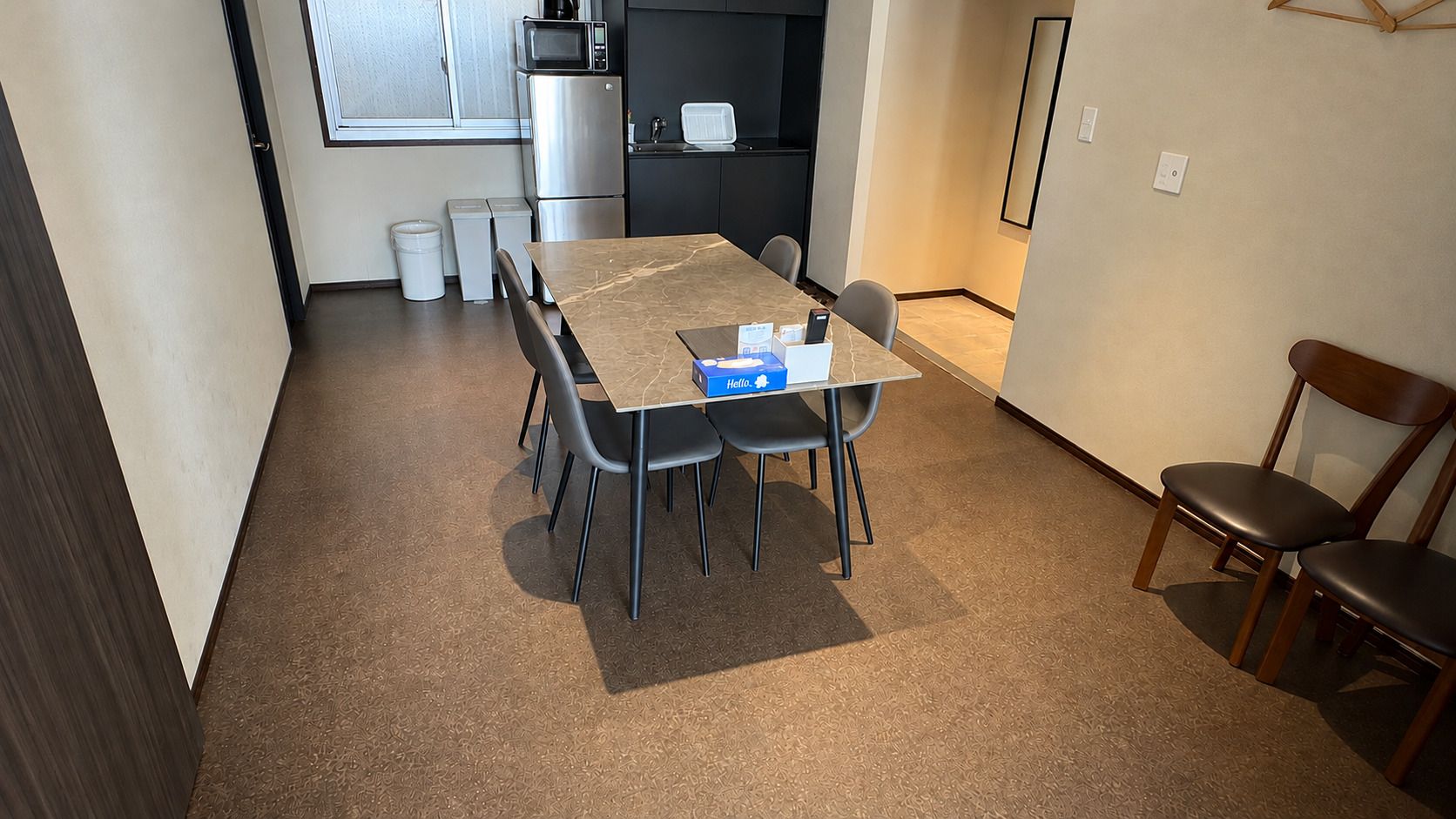 A compact dining area with a table and chairs, a microwave, and a refrigerator in the background.