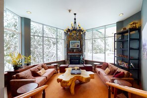 A spacious living room with a fireplace, large windows, and a chandelier. - Woodrun Lodge by Whistler Premier (Whistler)