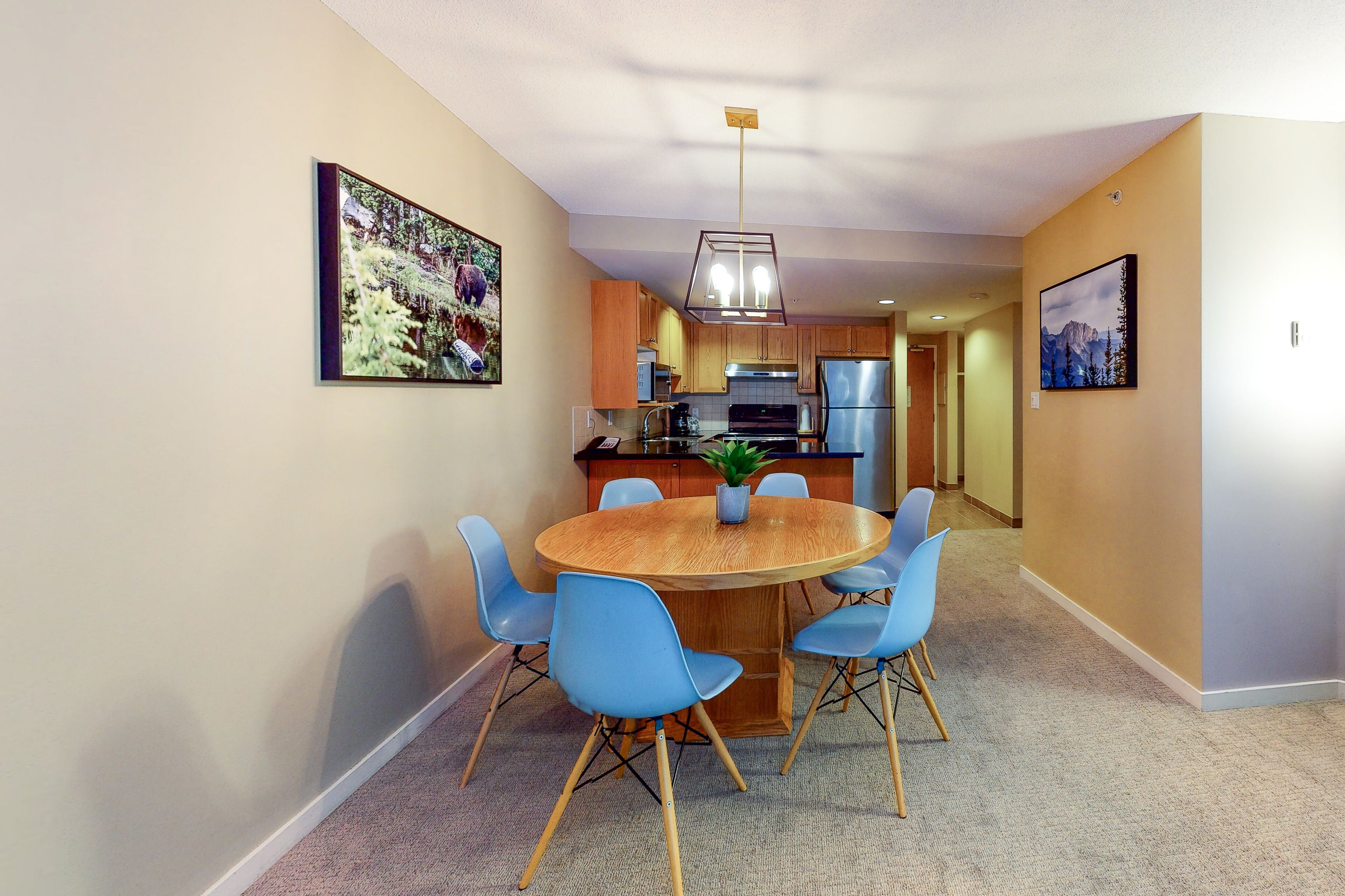 Een moderne keuken met houten kastjes, een roestvrijstalen koelkast, en een eethoek met een ronde tafel en blauwe stoelen.