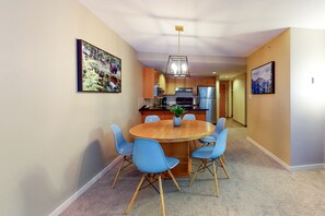 A modern kitchen with wooden cabinets, a stainless steel refrigerator, and a dining area with a round table and blue chairs. - Woodrun Lodge by Whistler Premier (Whistler)