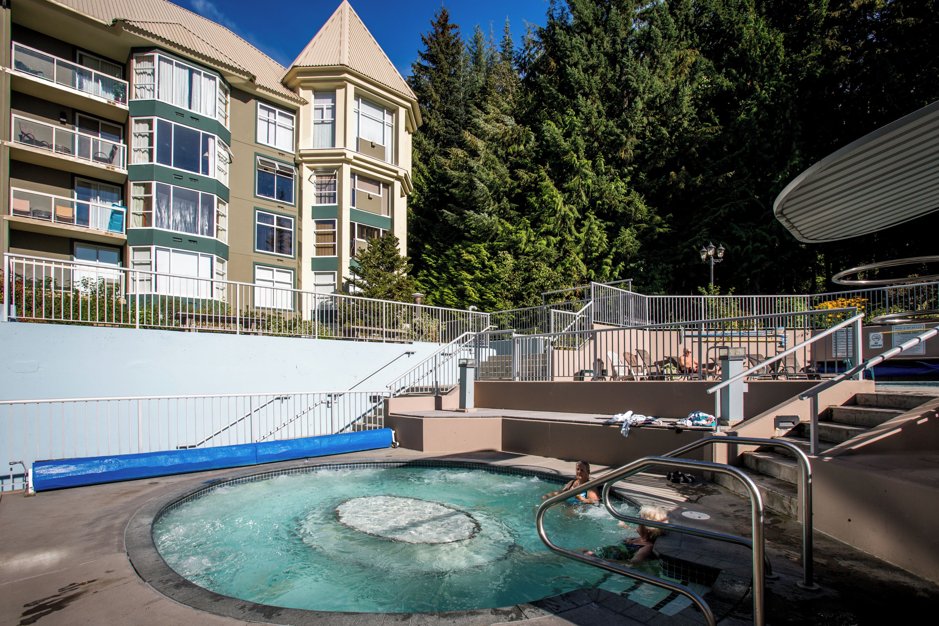 Una piscina de diseño circular, rodeada por una valla metálica, junto a un edificio de varios pisos con balcones.