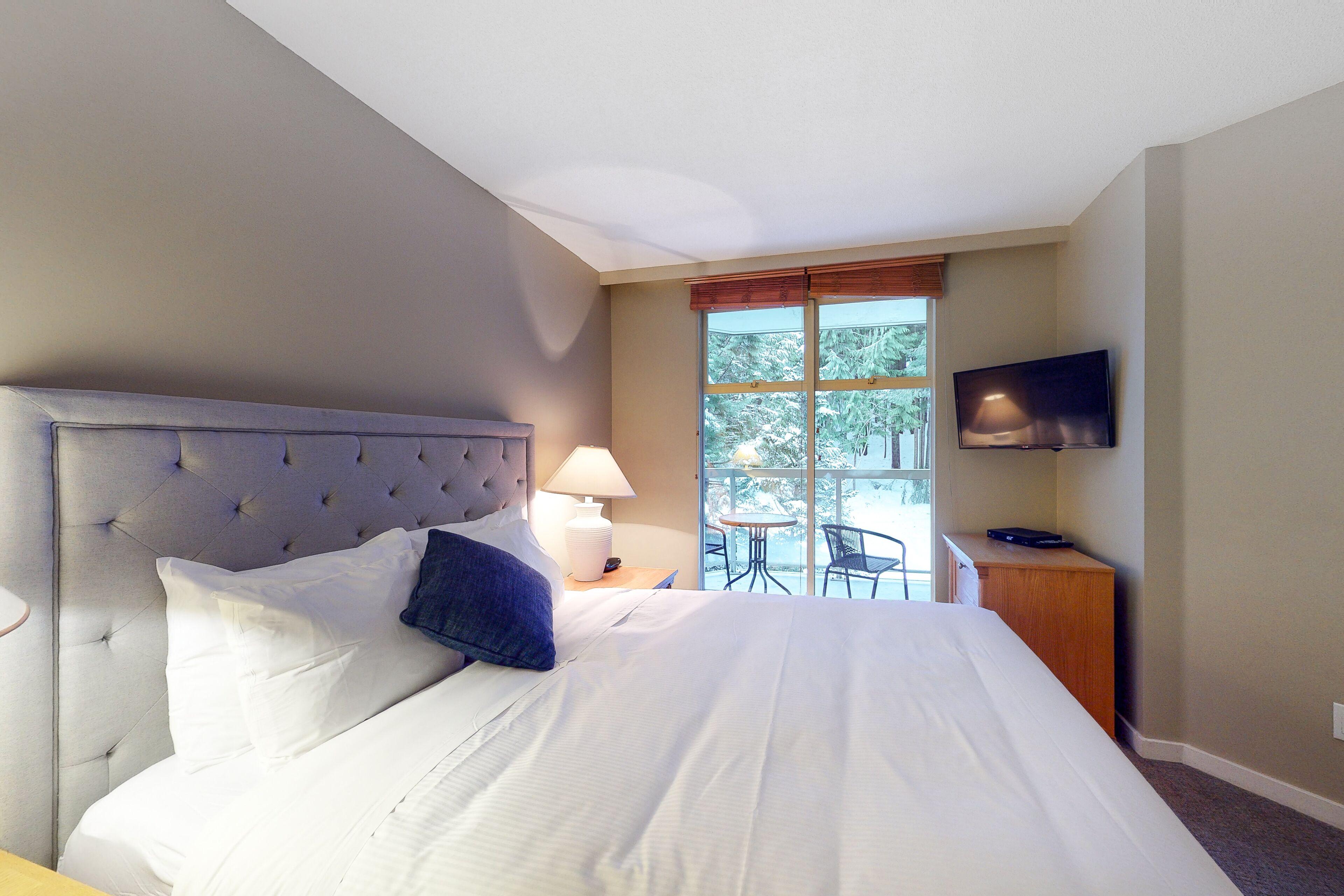 A hotel room with a large bed, a television, a window with a view, and a small table with chairs.