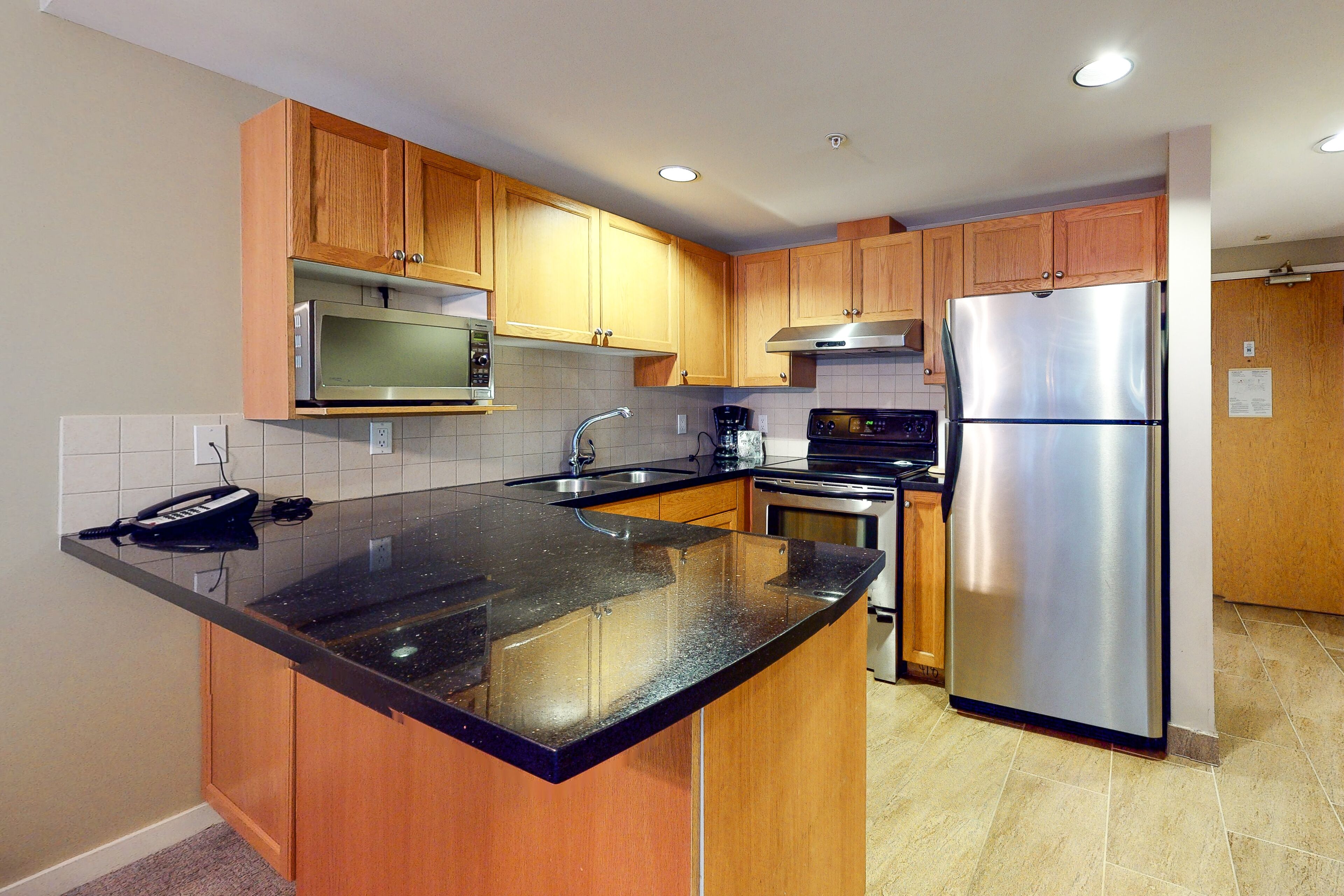 A modern kitchen with wooden cabinets, stainless steel appliances, and a black granite countertop.