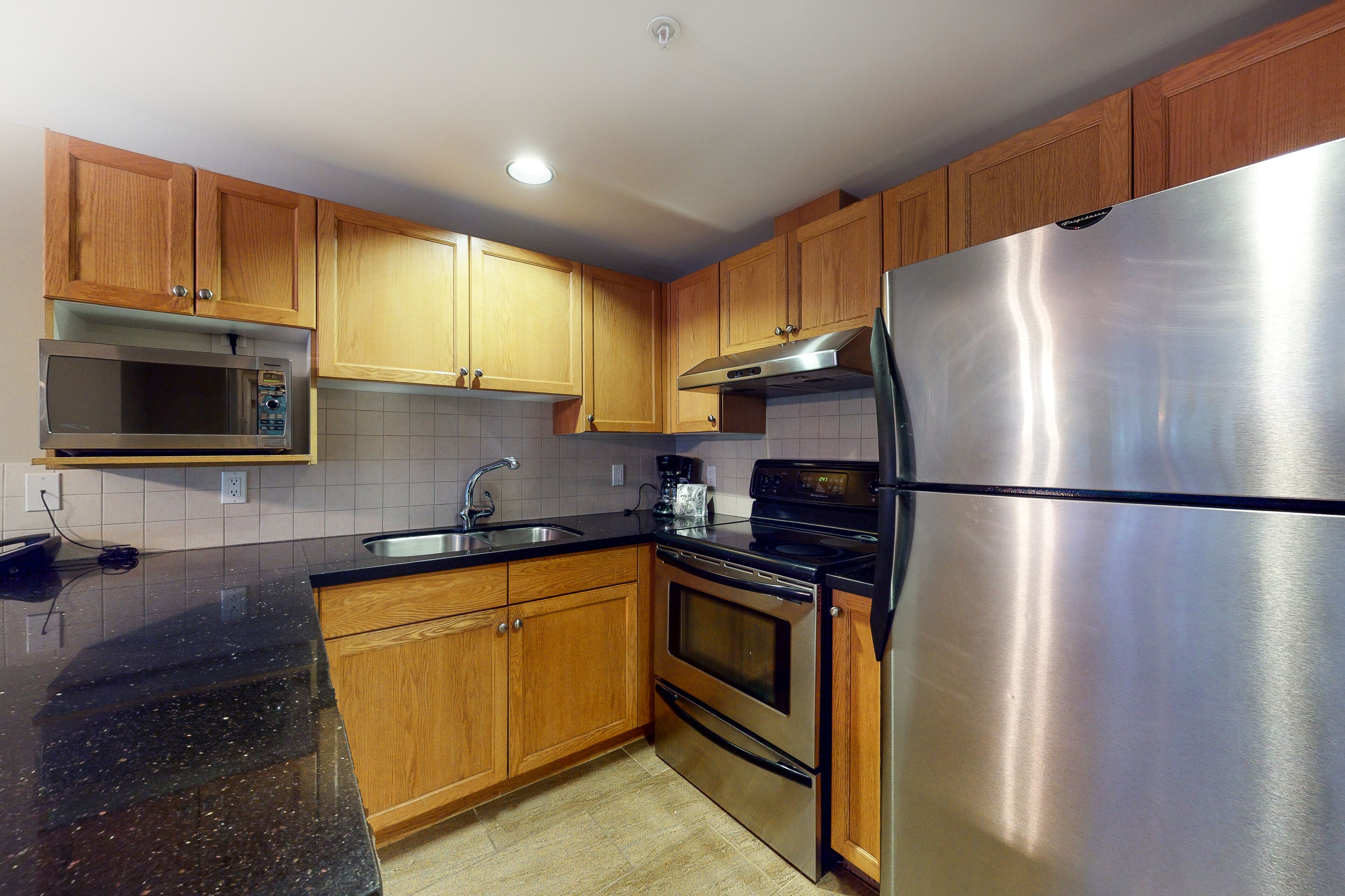 A kitchen with wooden cabinets, a stainless steel refrigerator, a microwave, and an oven.