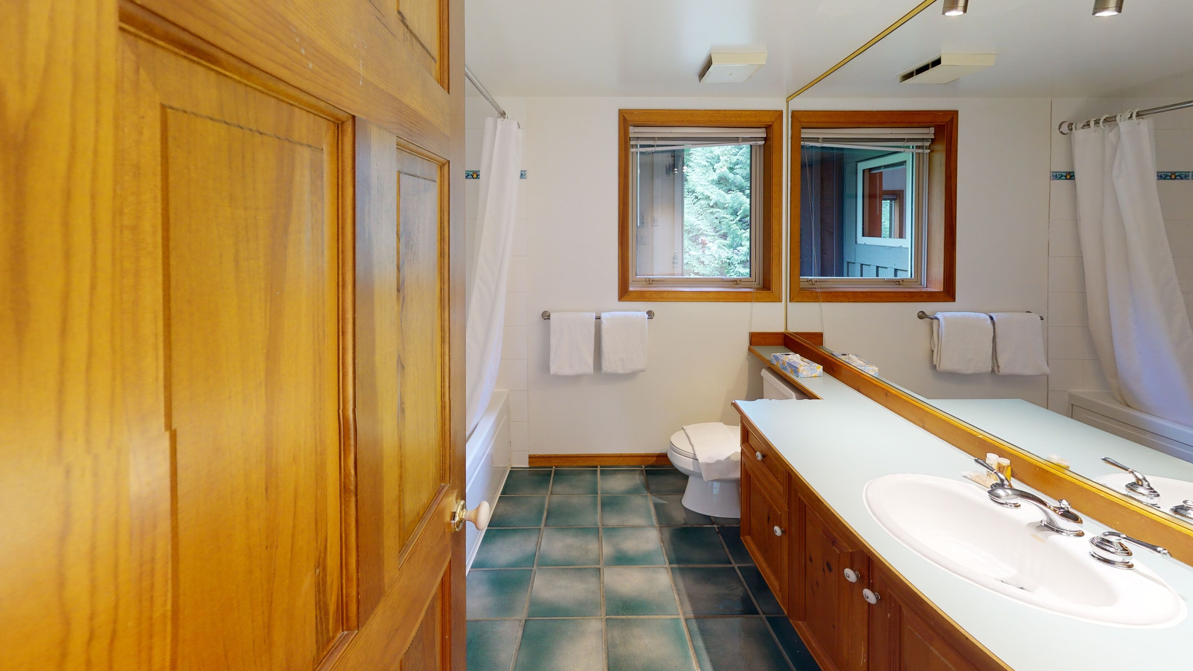 A bathroom with wooden cabinets, a white sink, a mirror, and a window with a view of trees.