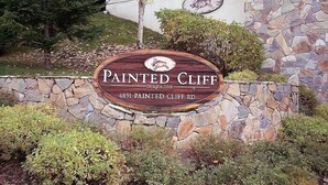A sign for Painted Cliff on Blackcomb, with a stone wall and greenery around. - Painted Cliff by Whistler Premier (Whistler)