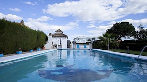 A swimming pool with a gazebo, surrounded by greenery and a clear sky.