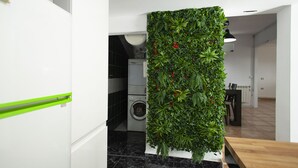 A kitchen with a vertical garden wall, a washing machine, and a dining area with a wooden table.