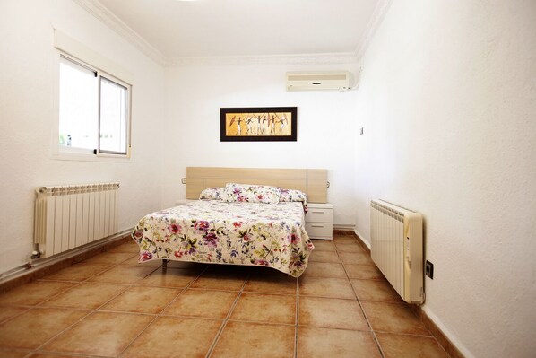 A bedroom with a bed, a nightstand, a radiator, and a window. - Villa with all amenities (Linares, Jaen)