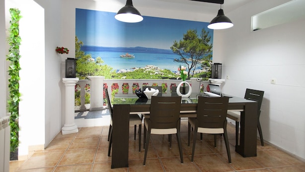 A dining area with a table and chairs, a mural of a coastal scene, and a view of the sea.