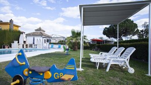 A poolside area with a children's play structure, lounge chairs, and a covered seating area.