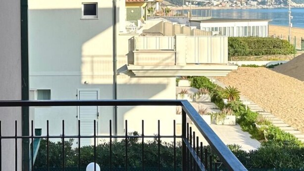 Een gebouw aan de kust met een balkon, uitzicht op de zee en een stad in de verte.