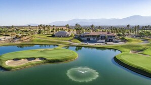 A golf course with a heart-shaped water feature, palm trees, and a large building with a sloped roof.