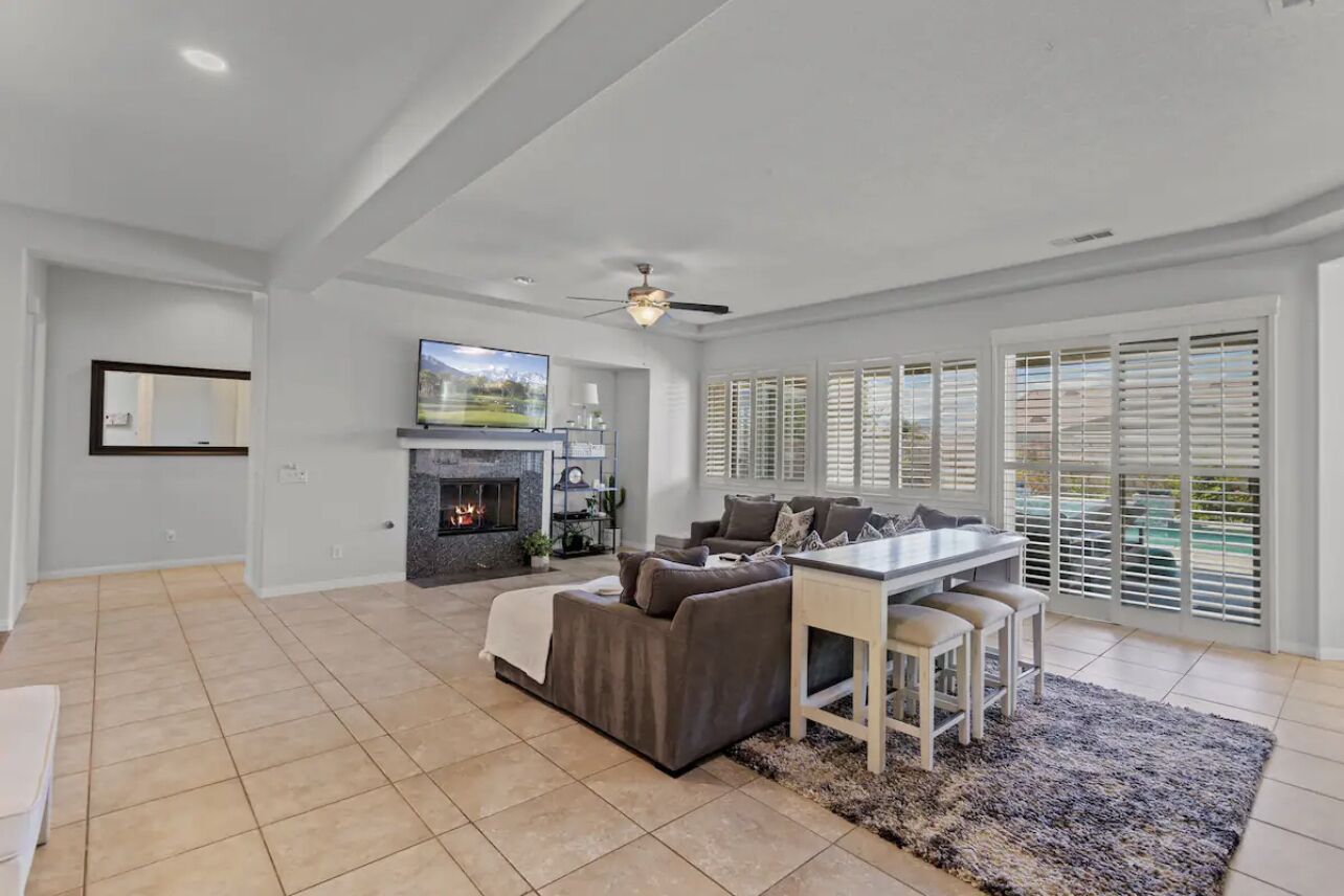 A spacious living room with a fireplace, a dining area, and large windows with blinds.