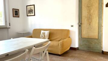 A room with a white table, a yellow sofa, a door with a decorative panel, and two framed pictures on the wall.