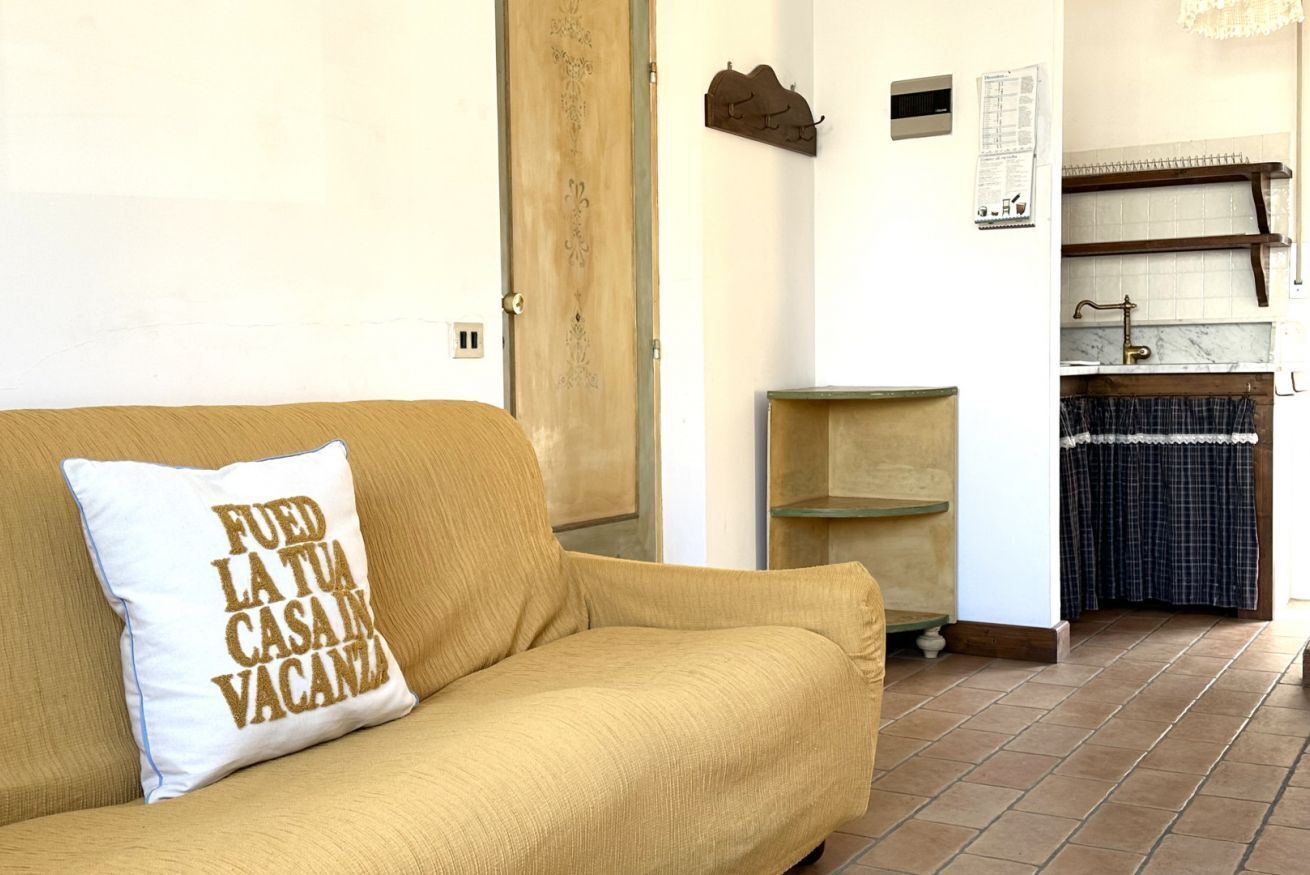 A beige sofa with a pillow, a wooden door, a small shelf, and a tiled floor.