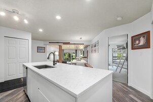 Una cocina moderna con una isla central, armarios blancos y vista al área de comedor contigua.