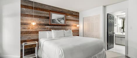 Ein Schlafzimmer mit einem großen Bett, einem Nachttisch, einer Holzwand und einer Tür zu einem Badezimmer.