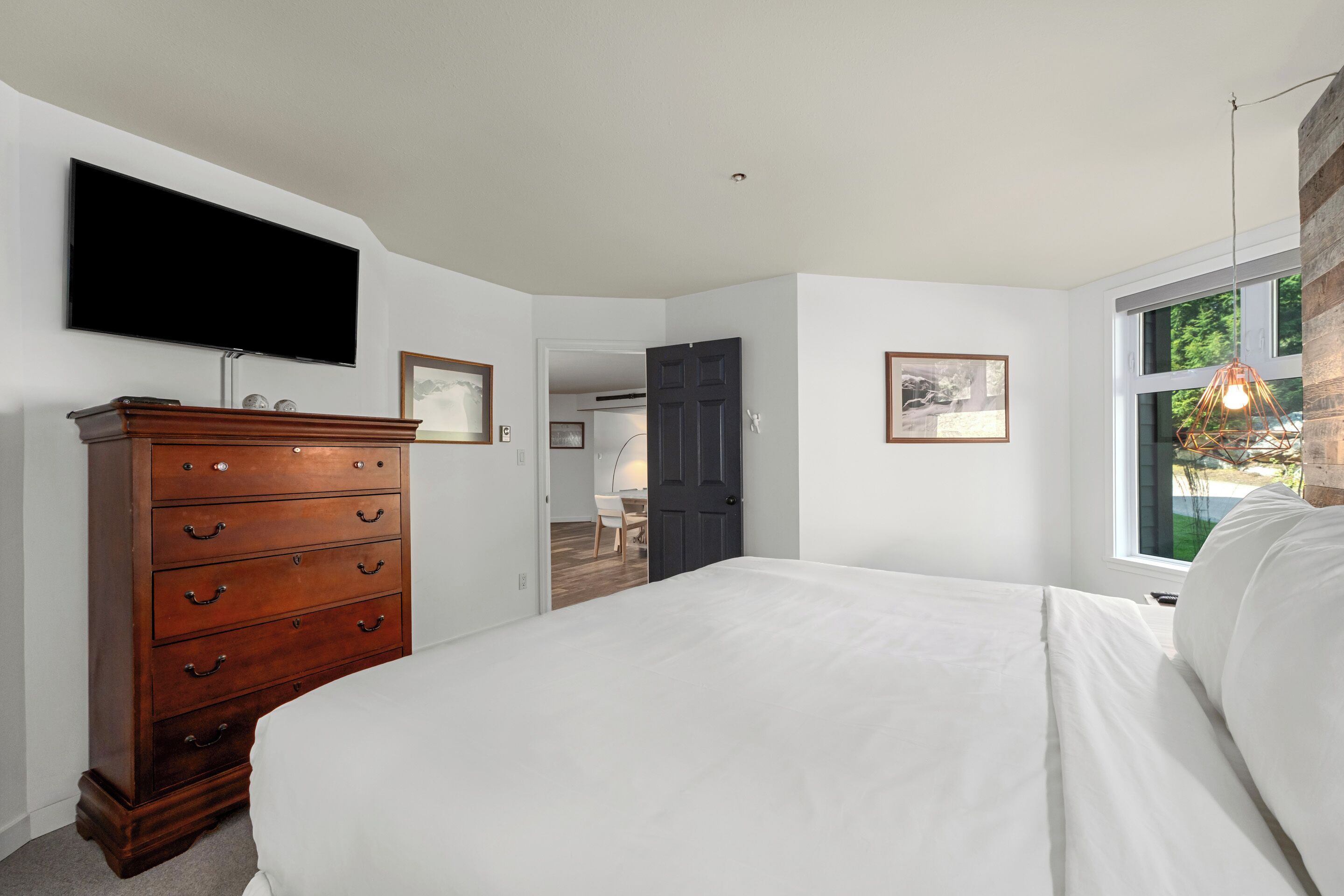 Een slaapkamer met een bed, een dressoir, een televisie en een raam met uitzicht.